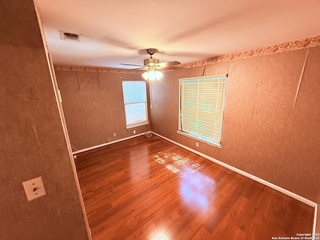 empty room with baseboards, wood finished floors, visible vents, and a ceiling fan