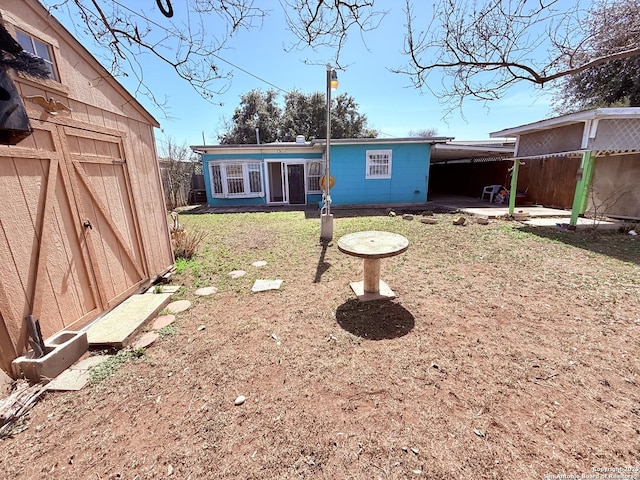 back of property with an attached carport, an outdoor structure, and fence