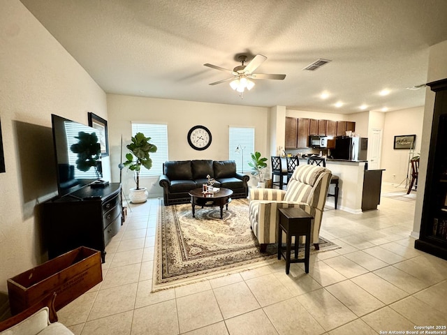 living room featuring light tile patterned floors, a textured ceiling, visible vents, and a ceiling fan