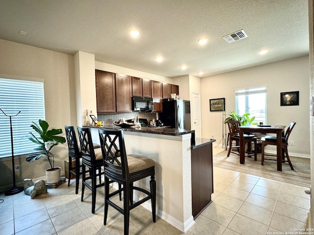 kitchen featuring light tile patterned floors, visible vents, freestanding refrigerator, a peninsula, and black microwave