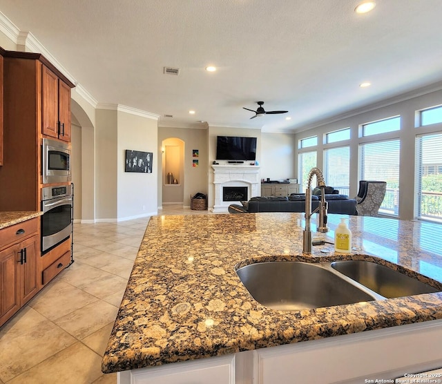 kitchen with a fireplace, a sink, appliances with stainless steel finishes, brown cabinets, and crown molding