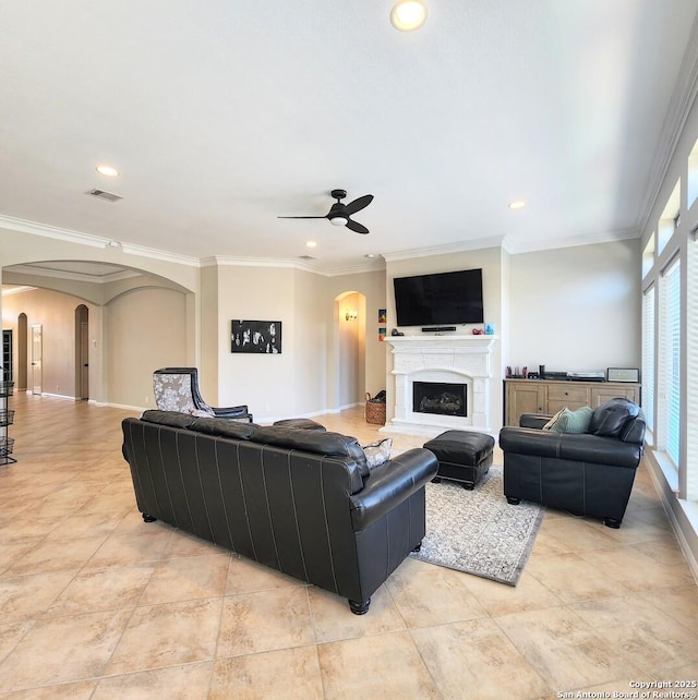 living room featuring arched walkways, a fireplace with raised hearth, visible vents, and crown molding