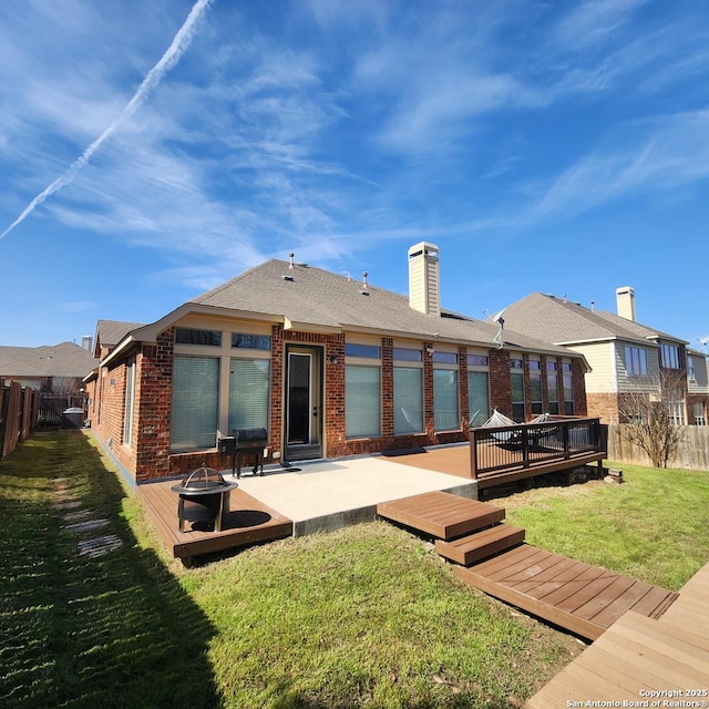 back of house featuring brick siding, a lawn, an outdoor fire pit, a deck, and a fenced backyard