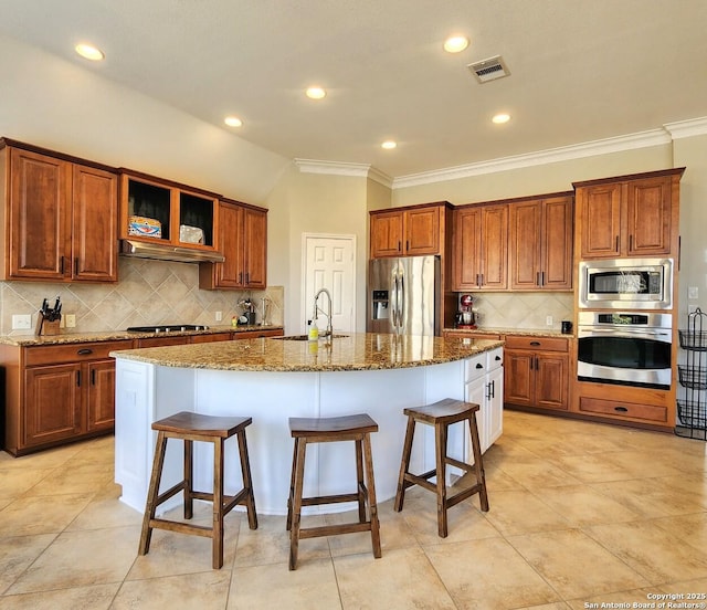 kitchen featuring stainless steel appliances, a sink, visible vents, brown cabinetry, and a kitchen bar