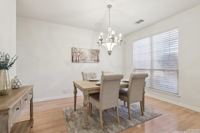 dining space with light wood finished floors, baseboards, visible vents, and an inviting chandelier