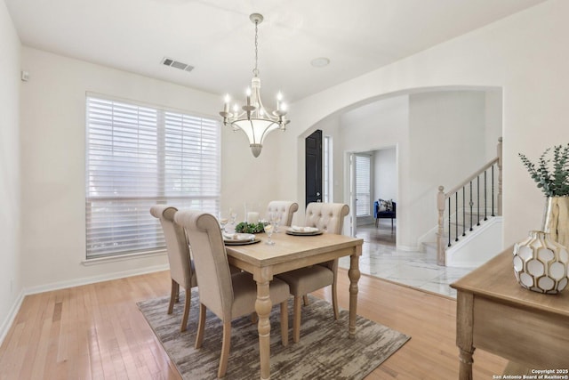 dining area with baseboards, visible vents, arched walkways, an inviting chandelier, and stairs