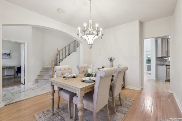 dining area with arched walkways, a notable chandelier, light wood-style flooring, baseboards, and stairs