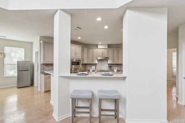 kitchen featuring light wood finished floors, a breakfast bar area, visible vents, decorative backsplash, and appliances with stainless steel finishes