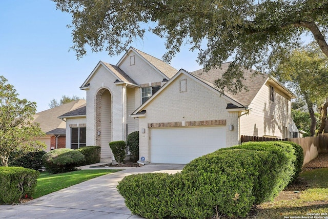 traditional-style home featuring a garage, brick siding, fence, concrete driveway, and roof with shingles