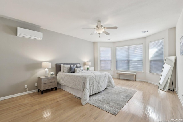 bedroom featuring a wall unit AC, light wood finished floors, visible vents, a ceiling fan, and baseboards