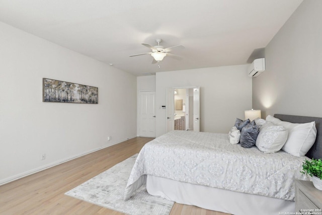 bedroom featuring baseboards, connected bathroom, a ceiling fan, a wall unit AC, and wood finished floors