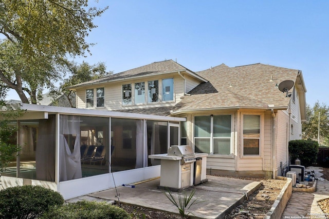 rear view of house featuring a shingled roof, a sunroom, and a patio