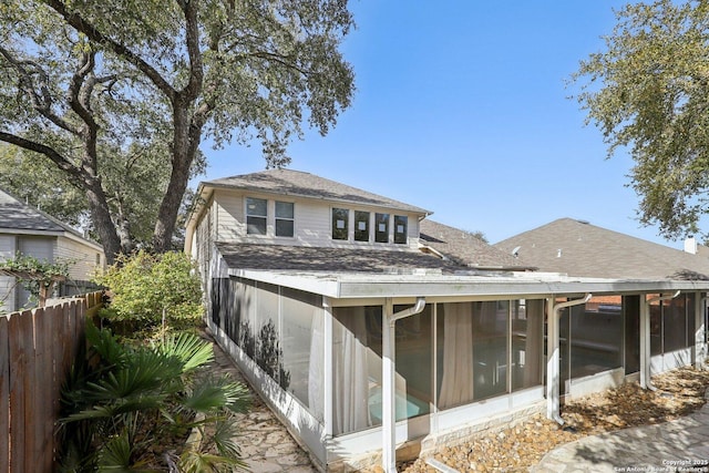 rear view of house with a sunroom, roof with shingles, and fence