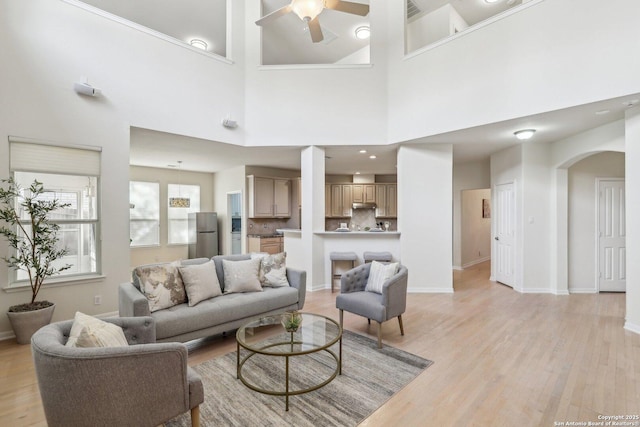 living area with arched walkways, light wood-style flooring, visible vents, baseboards, and a ceiling fan