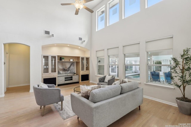 living room with ceiling fan, arched walkways, visible vents, baseboards, and light wood finished floors