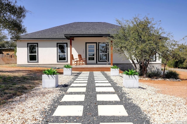 view of front facade featuring covered porch, roof with shingles, and stucco siding