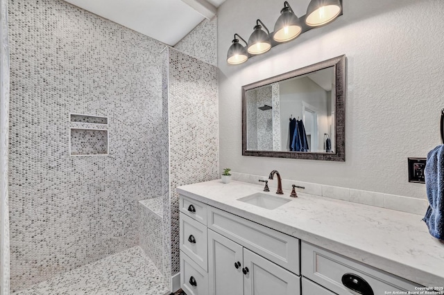 bathroom featuring a textured wall, tiled shower, and vanity