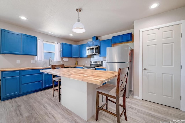 kitchen with light wood finished floors, appliances with stainless steel finishes, a breakfast bar, blue cabinetry, and wooden counters