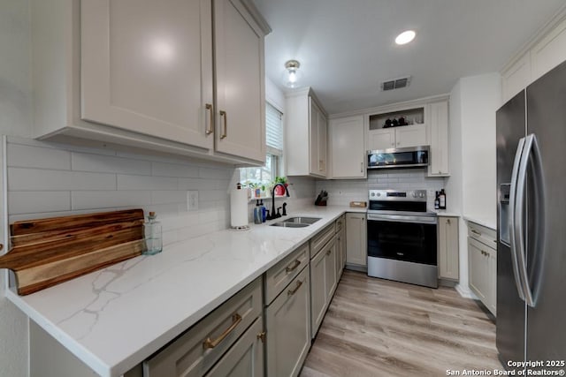 kitchen with visible vents, backsplash, light wood-style flooring, appliances with stainless steel finishes, and a sink