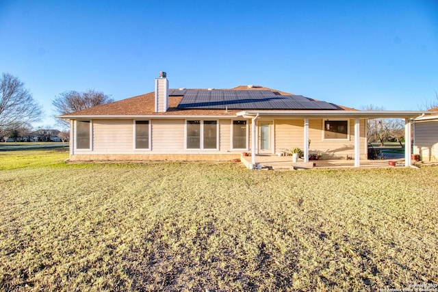 back of property featuring a yard, a patio, a chimney, and solar panels