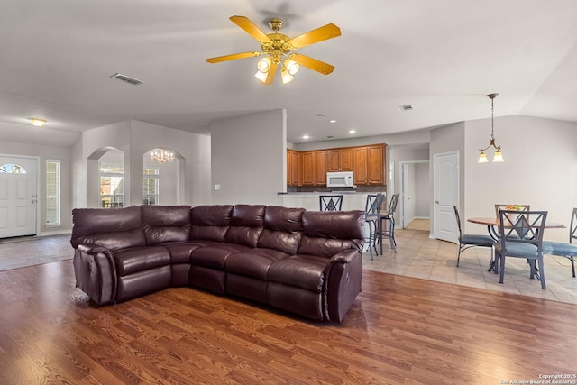 living area featuring lofted ceiling, light wood-style flooring, ceiling fan with notable chandelier, and visible vents