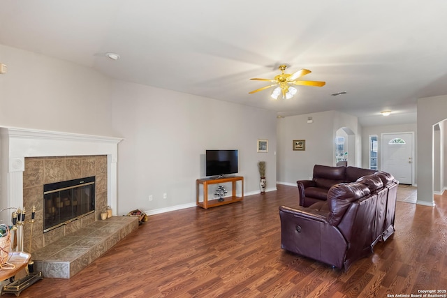 living area with a tiled fireplace, baseboards, arched walkways, and dark wood-type flooring