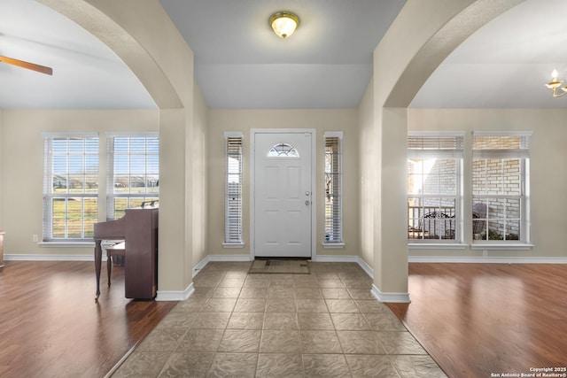 foyer featuring arched walkways, wood finished floors, a ceiling fan, baseboards, and vaulted ceiling