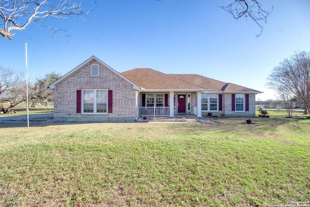 ranch-style home featuring covered porch, a shingled roof, a front yard, and brick siding