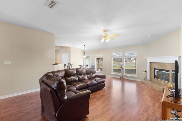 living area featuring a tile fireplace, visible vents, baseboards, and wood finished floors