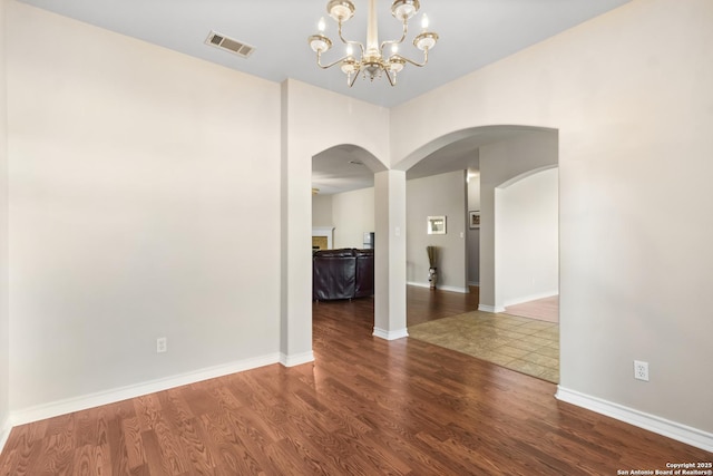 unfurnished room with arched walkways, wood finished floors, visible vents, baseboards, and an inviting chandelier