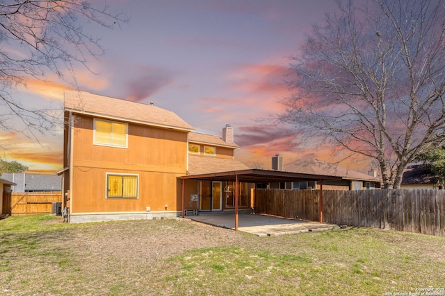 back of property at dusk with a patio area, a yard, a chimney, and fence