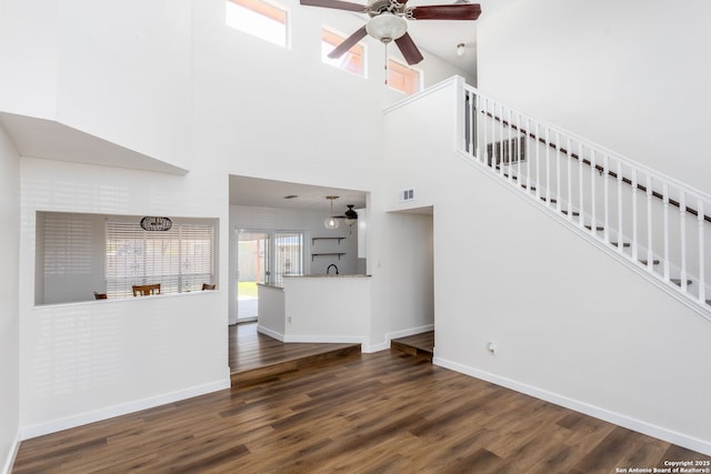 unfurnished living room featuring visible vents, a ceiling fan, wood finished floors, baseboards, and stairs