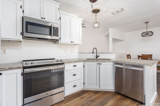 kitchen with white cabinets, dark wood-style flooring, a peninsula, stainless steel appliances, and a sink