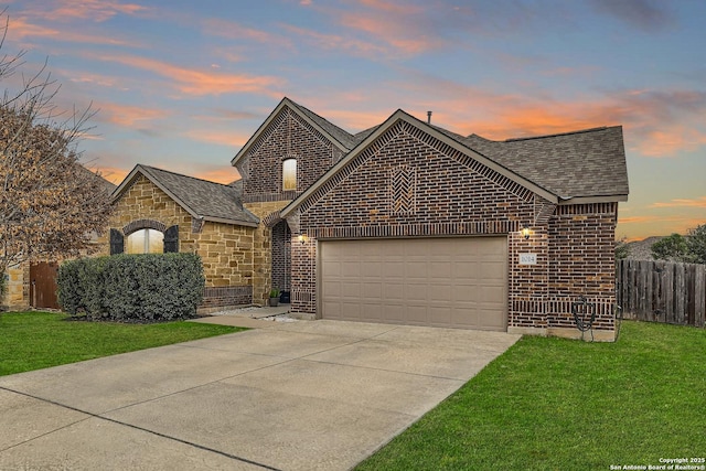 french provincial home with an attached garage, brick siding, fence, driveway, and a lawn