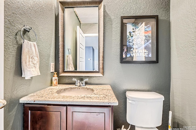 half bath featuring toilet, vanity, and a textured wall