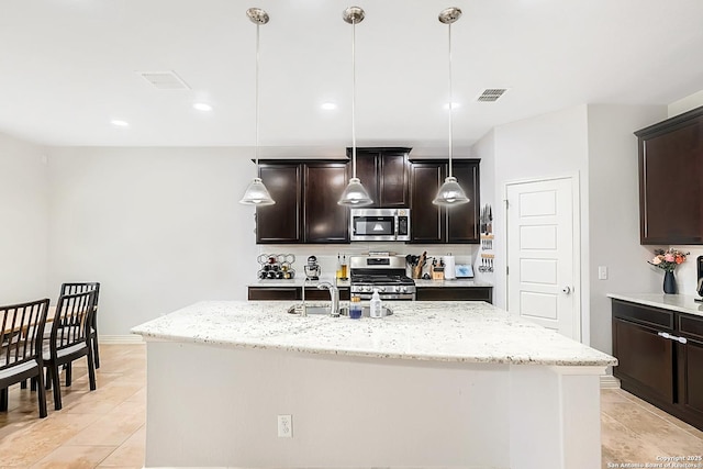 kitchen with a kitchen island with sink, visible vents, stainless steel appliances, and decorative light fixtures