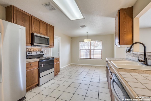 kitchen with tile counters, electric stove, stainless steel microwave, freestanding refrigerator, and a sink