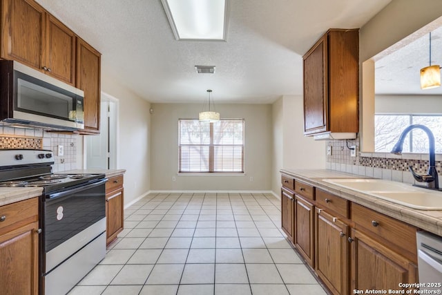 kitchen with light tile patterned floors, appliances with stainless steel finishes, brown cabinetry, a sink, and baseboards