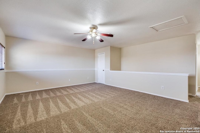 carpeted spare room with ceiling fan, a textured ceiling, attic access, and baseboards