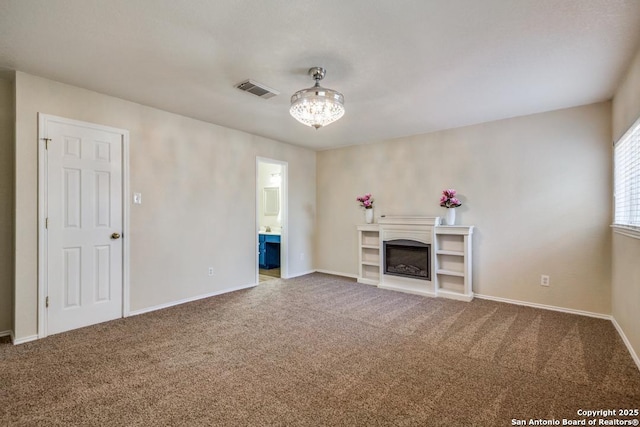 unfurnished living room with carpet flooring, a glass covered fireplace, visible vents, and baseboards