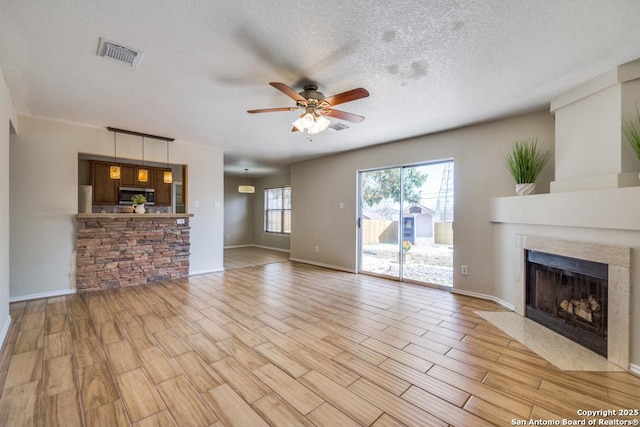 unfurnished living room with light wood finished floors, visible vents, a fireplace with flush hearth, ceiling fan, and a textured ceiling