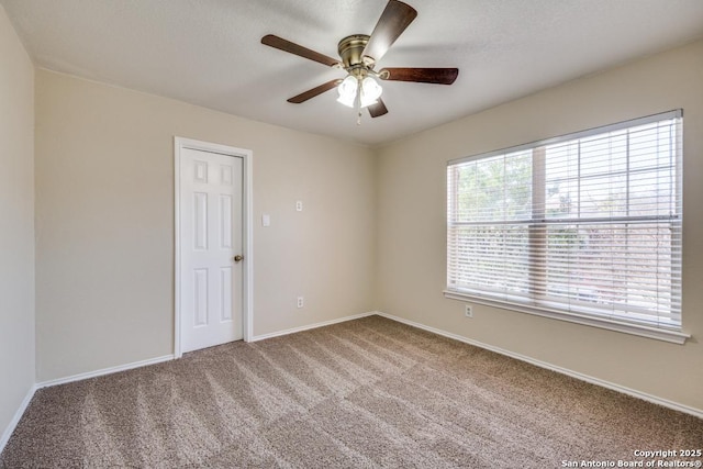 carpeted empty room featuring a ceiling fan and baseboards