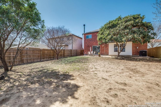 rear view of house featuring brick siding, cooling unit, and a fenced backyard