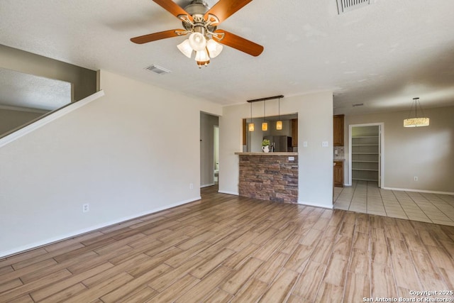 unfurnished living room with light wood finished floors, ceiling fan, visible vents, and baseboards