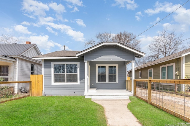 view of front of home featuring a front yard, covered porch, roof with shingles, and fence