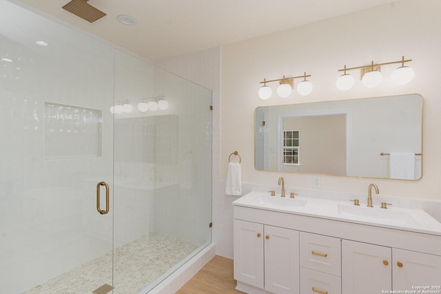 bathroom with double vanity, wood finished floors, a stall shower, and a sink