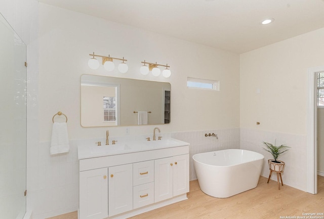 bathroom featuring double vanity, a soaking tub, a sink, and wood finished floors