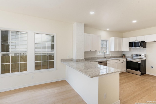 kitchen featuring light wood-style flooring, light stone counters, a sink, stainless steel appliances, and backsplash