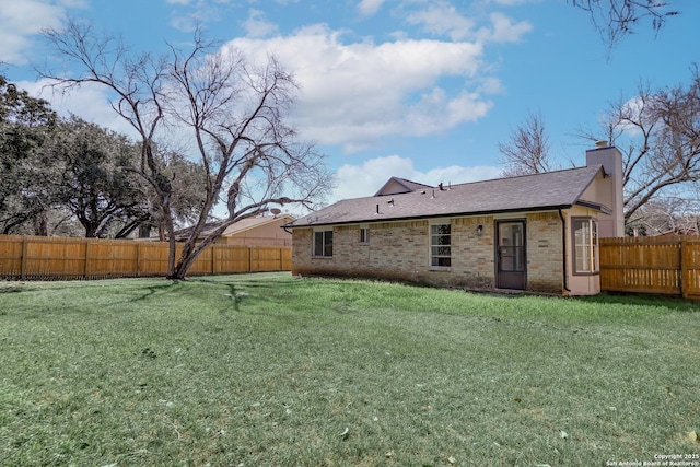 back of house featuring a yard, brick siding, a chimney, and a fenced backyard