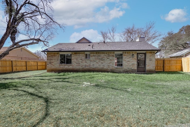 back of property with brick siding, a lawn, a chimney, and a fenced backyard